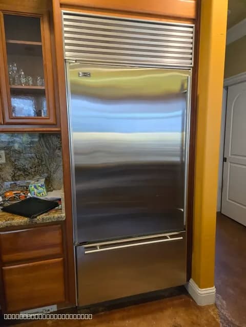 Stainless steel Sub-Zero refrigerator installed in custom wood cabinetry, showcasing high-end appliance service.
